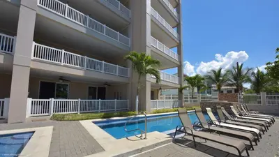 a row of lounge chairs next to a building with a swimming pool at The Palms Jaco in Jacó