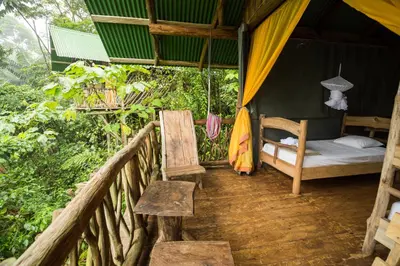 a bed and a chair in a tent in the woods at La Tigra Rainforest Lodge in Fortuna