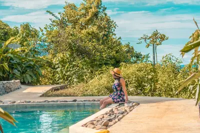 a woman sitting on a rock by a swimming pool at La Tigra Rainforest Lodge in Fortuna