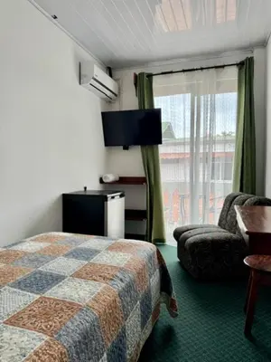 a hotel room with a bed and a chair and a window at Hotel Malinche in Quepos