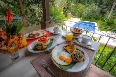 a table with plates of breakfast food on a balcony at La Finca Lodge in Fortuna