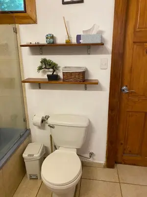 a bathroom with a toilet and shelves on the wall at Casa Piscina in Santa Teresa Beach