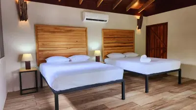 two beds in a room with white sheets at Boca Tapada Lodge in Boca Tapada