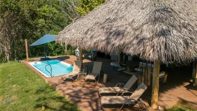 a swimming pool with chairs and a thatched roof at Isla Chiquita Glamping Hotel in Puntarenas