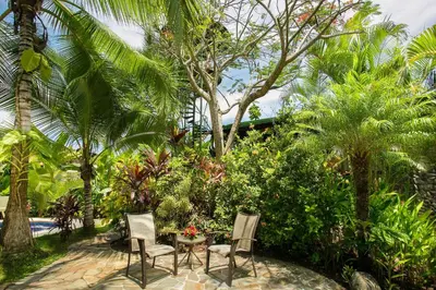 two chairs and a table in a garden with palm trees at Villas Oasis in Manuel Antonio