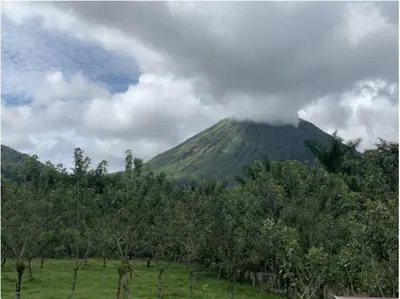 a mountain with clouds on top of it with trees at Aunty Arenal Lodge in Fortuna