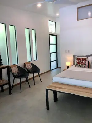 a bedroom with a bed and two chairs and windows at Rancho Capulin B&B in Tarcoles