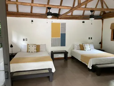 two beds in a room with white walls and wooden ceilings at Rancho Capulin B&B in Tarcoles