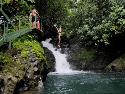 two people jumping off of a waterfall into a river at Santa Juana Lodge & Nature Reserve in Quepos