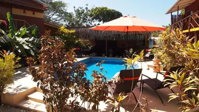 a swimming pool with an umbrella next to a house at Samara Palm Lodge in Sámara