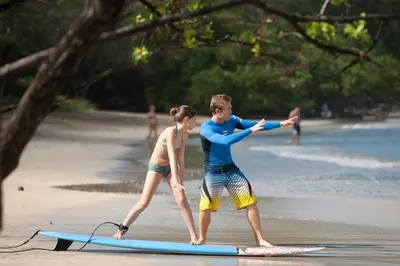 a boy and a girl on a surfboard on the beach at The Breeze Hotel & Villas in Tamarindo