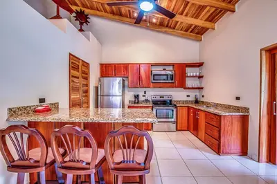 a kitchen with wooden cabinets and a island with chairs at Hidden Palms in Nosara