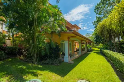 a yellow house with a green yard at Colina 9E 2 bdr Garden View in Los Suenos in Herradura