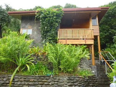 a small cabin with a porch and a stone wall at Arco Iris Lodge in Monteverde Costa Rica