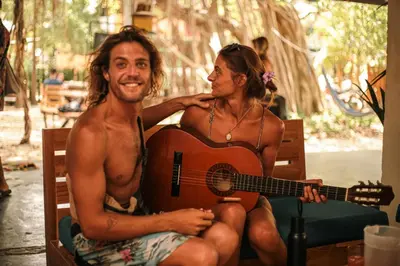 a man and a woman sitting in a chair with a guitar at Zeneidas Surf Garden in Santa Teresa Beach