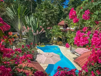 a resort pool with an umbrella and pink flowers at The Scarlet Villas in Ojochal