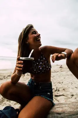 a woman sitting on the beach holding a drink at Peace Lofts and Apartments in Santa Teresa Beach