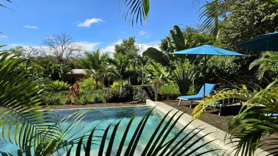 a swimming pool with a chair and an umbrella at Tee-K Lodge Tamarindo in Tamarindo