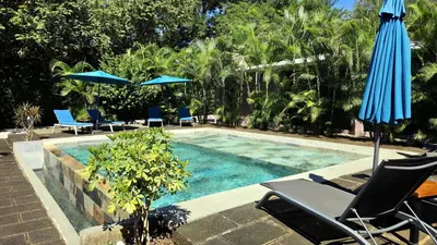 a swimming pool with chairs and umbrellas next to at Tee-K Lodge Tamarindo in Tamarindo