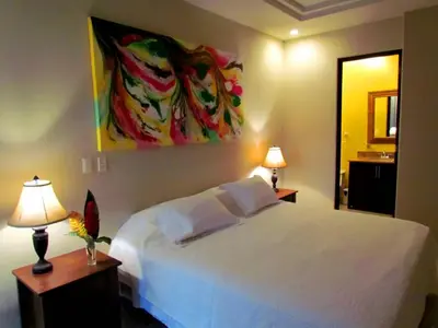 a bedroom with a white bed with two lamps and a painting at Tamarindo Condo 206 Matapalo in Tamarindo