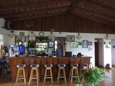 a bar with stools and a man standing behind it at Hotel La Rana de Arenal in Nuevo Arenal