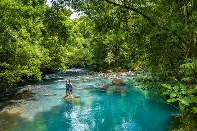 two people standing on a rock in a river at Hideaway Rio Celeste Hotel in Bijagua