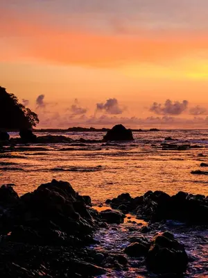 a sunset over the ocean with rocks in the water at Casas Mal Pais in Mal País