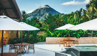 a patio with tables and umbrellas with a mountain in the background at Nayara Gardens in Fortuna