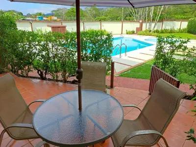 a glass table and chairs with an umbrella next to a pool at Rio Copey 2 townhouse near the beach in Jaco in Jacó