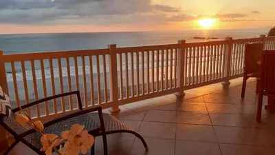a balcony with a view of the beach at sunset at The Palms Jaco 1001 penthouse on the beach in Jacó