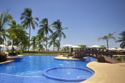 a bridge over a swimming pool with palm trees at The Palms Jaco 1001 penthouse on the beach in Jacó