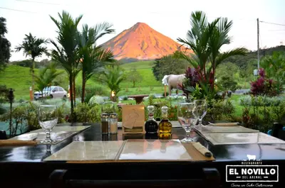 a table with wine glasses and a mountain in the background at Lumbres Arenal in Fortuna