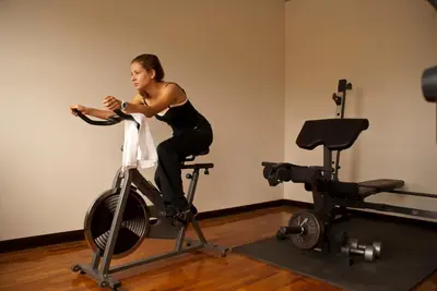 a woman riding a exercise bike in a gym at Hotel Plaza Real Suites & Apartments San Jose in San José
