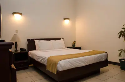 a bedroom with a large bed with white sheets and pillows at Hotel Plaza Real Suites & Apartments San Jose in San José