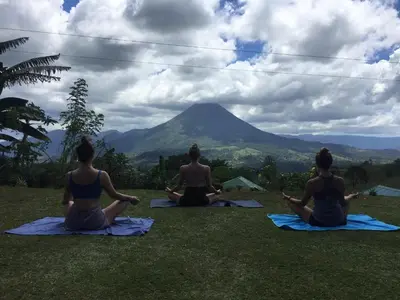 a group of people sitting in a yoga pose in front of a mountain at Casa Torre Eco- Lodge in Fortuna