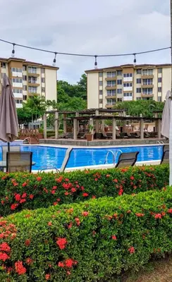 a swimming pool with chairs and flowers in front of a building at Jaco Beach Penthouse in Jacó
