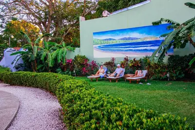 three people sitting on benches in the grass in front of a painting at Hotel Giada in Sámara