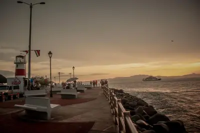 a pier with benches and a lighthouse on the water at Hotel Yadran Beach Resort in Puntarenas