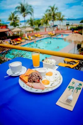 a plate of food on a table next to a pool at Hotel Yadran Beach Resort in Puntarenas