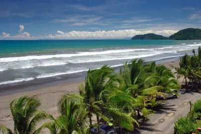 a view of a beach with palm trees and the ocean at Bahia Azul 2A beachfront, Jaco Beach, 1st floor in Jacó