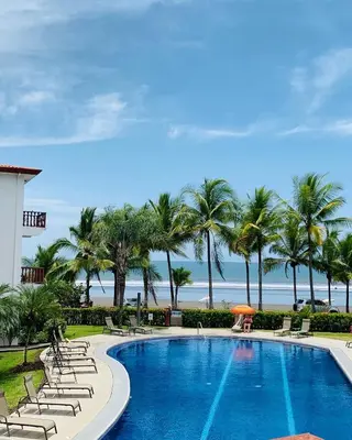 a swimming pool with chairs and palm trees and the ocean at Bahia Azul 2A beachfront, Jaco Beach, 1st floor in Jacó
