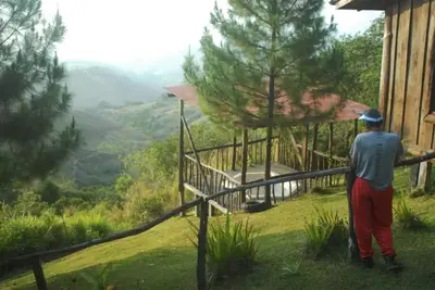 a man standing outside of a cabin looking at a valley at Cabañas Don Camilo Albergue de Montaña in Cabecera de Cañas
