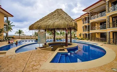 a resort with a swimming pool with a straw umbrella at Bahia Encantada beach front proyect, Micasas in Jacó
