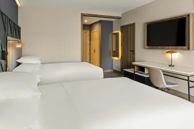 two beds in a hotel room with a desk and a tv at Courtyard by Marriott San Jose Escazu in San José