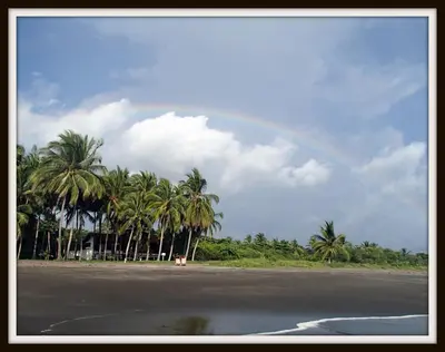 a rainbow in the sky over a beach with palm trees at Plumita Pacifica in Playa Junquillal