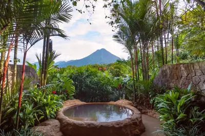 a garden with a bath tub with a mountain in the background at The Springs Resort & Spa at Arenal in Fortuna