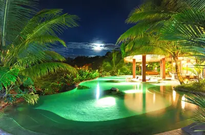 a pool in a resort at night with palm trees at The Springs Resort & Spa at Arenal in Fortuna