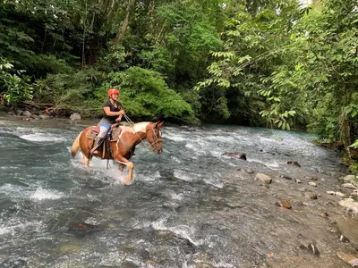 a woman riding a horse through a river at Hotel SueñoReal RioCeleste in Rio Celeste