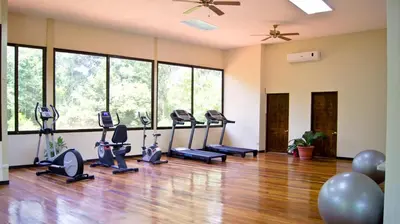 a gym with treadmills and ellipticals in a room with windows at Hotel San Bada Resort & Spa in Manuel Antonio