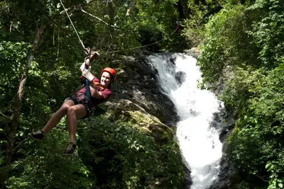 a man on a zip line in front of a waterfall at Adventure Park & Hotel Vista Golfo in Tajo Alto